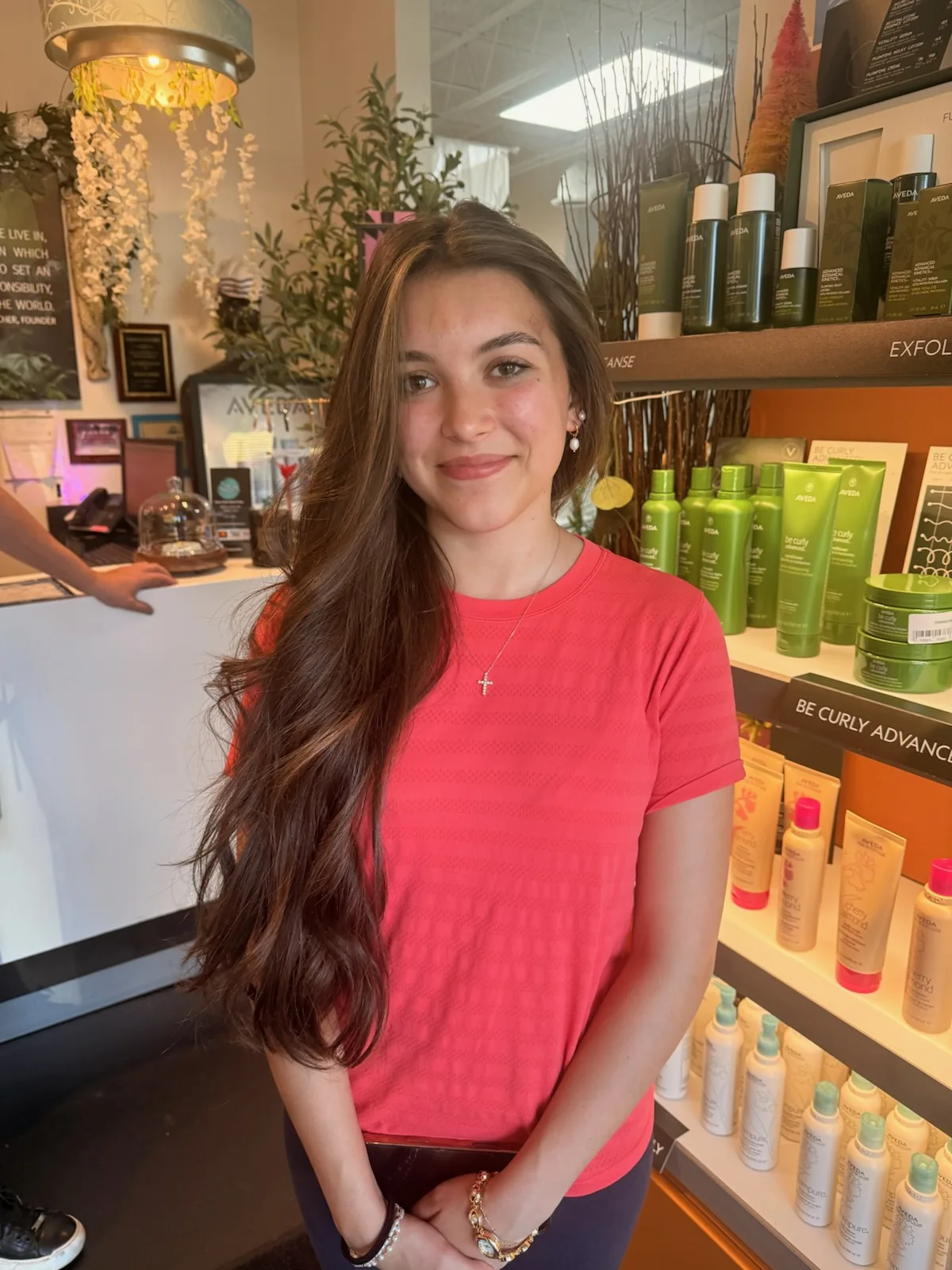 Aqua Aveda Salon & Spa team member standing beside shelves of Aveda retail products in the salon