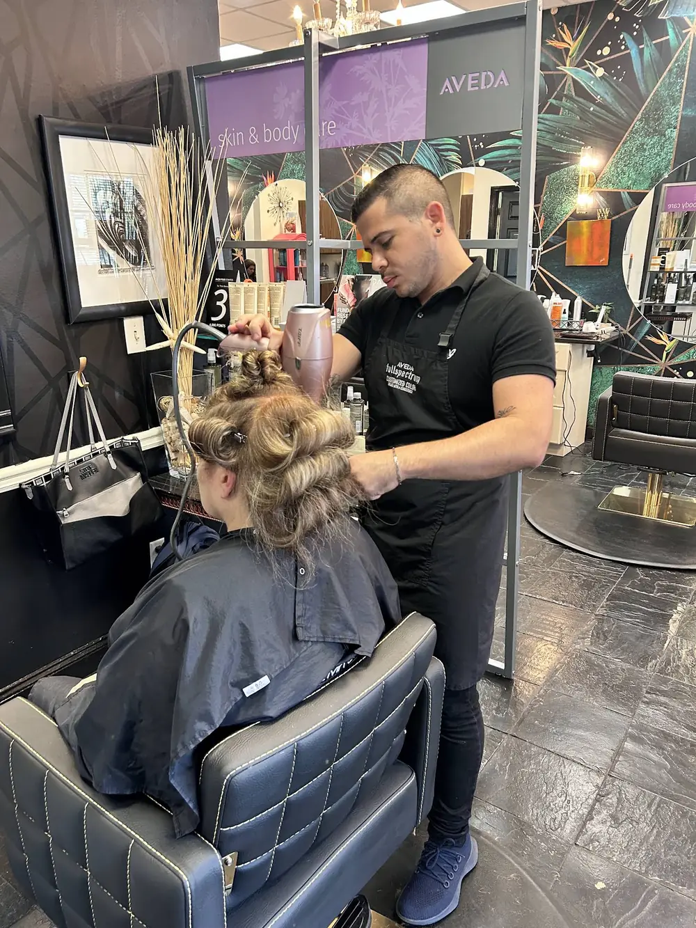 Stylist finishing a client's hair at an Aveda-branded station inside Aqua Aveda Salon & Spa