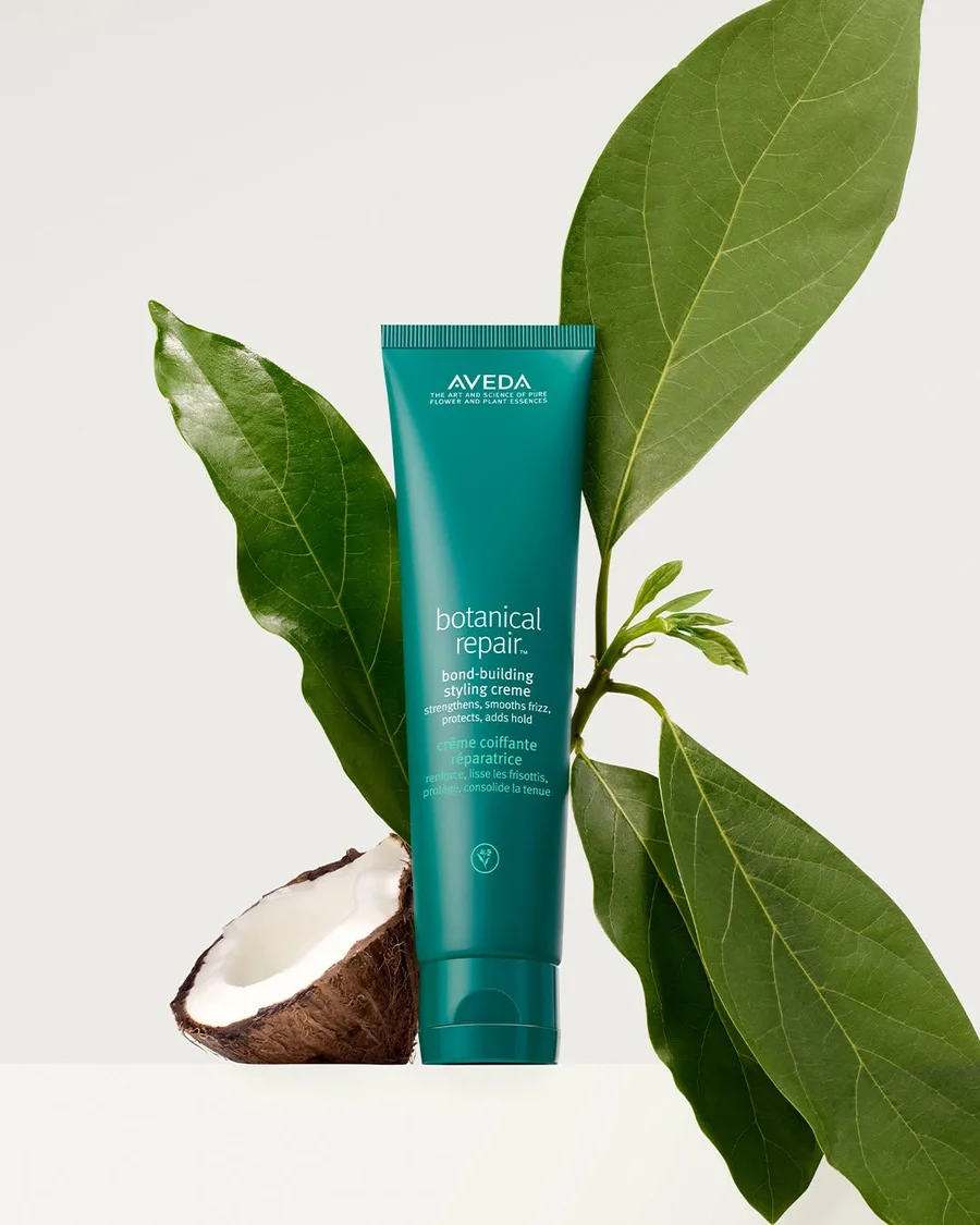 Aveda Botanical Repair styling creme beside a halved coconut and glossy green leaves